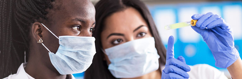 Two researchers in masks and gloves examine the contents of a vial together.