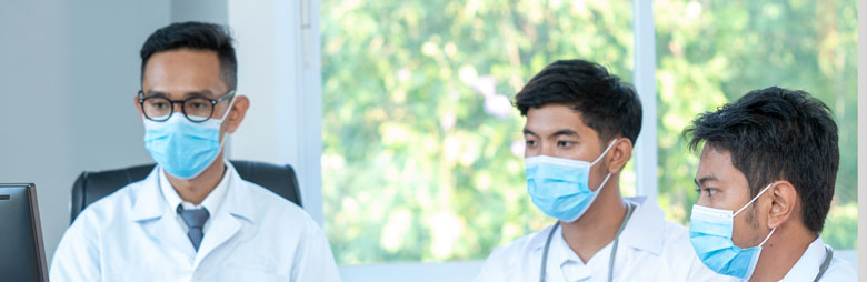 Three health professionals in masks focusing on important data displayed on a computer screen.